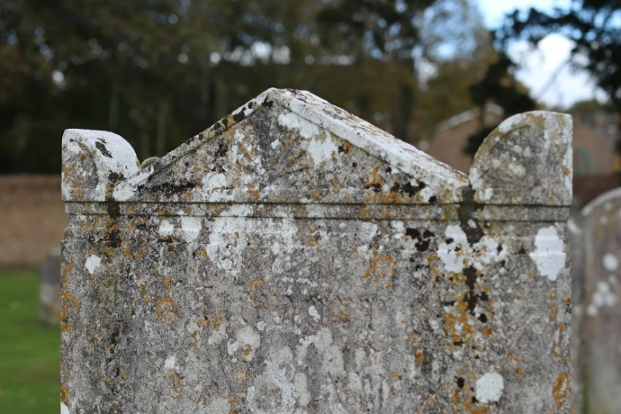 Close up of a weathered stone tombstone with lichen.
